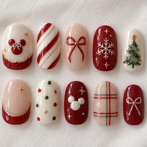 Puede incluir: Un juego de diez uñas postizas con diseños navideños que incluyen un icono rojo de Mickey Mouse, rayas de bastón de caramelo, lazos rojos, copos de nieve blancos, un árbol de Navidad verde, lunares rojos y verdes y un patrón de cuadros.