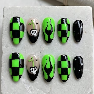 May include: A set of ten almond-shaped press-on nails featuring a black and neon green checkerboard pattern, a nude base with a black cherry skull design, neon green flames on a black background, and a black base with white star and dot accents.