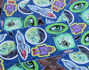 May include: A set of colorful stickers featuring space-themed illustrations. The stickers include robots, planets, eyes, and a bug with a glowing body. The stickers are printed on white paper with a blue background.
