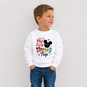 A young boy wearing a white sweatshirt with a Disney-themed design and text.
