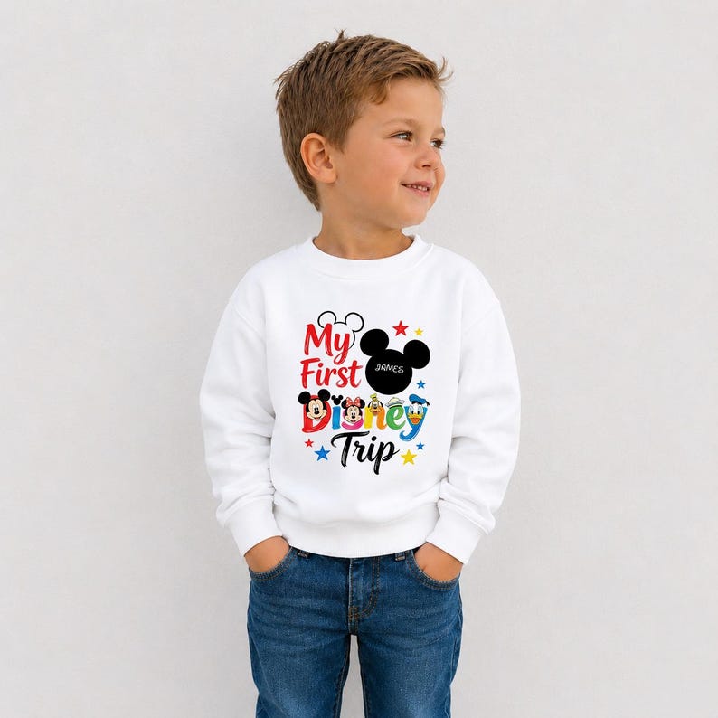 A young boy wearing a white sweatshirt with a Disney-themed design and text.