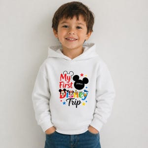 A young boy wearing a white hoodie with a Disney-themed graphic and text, smiling at the camera.