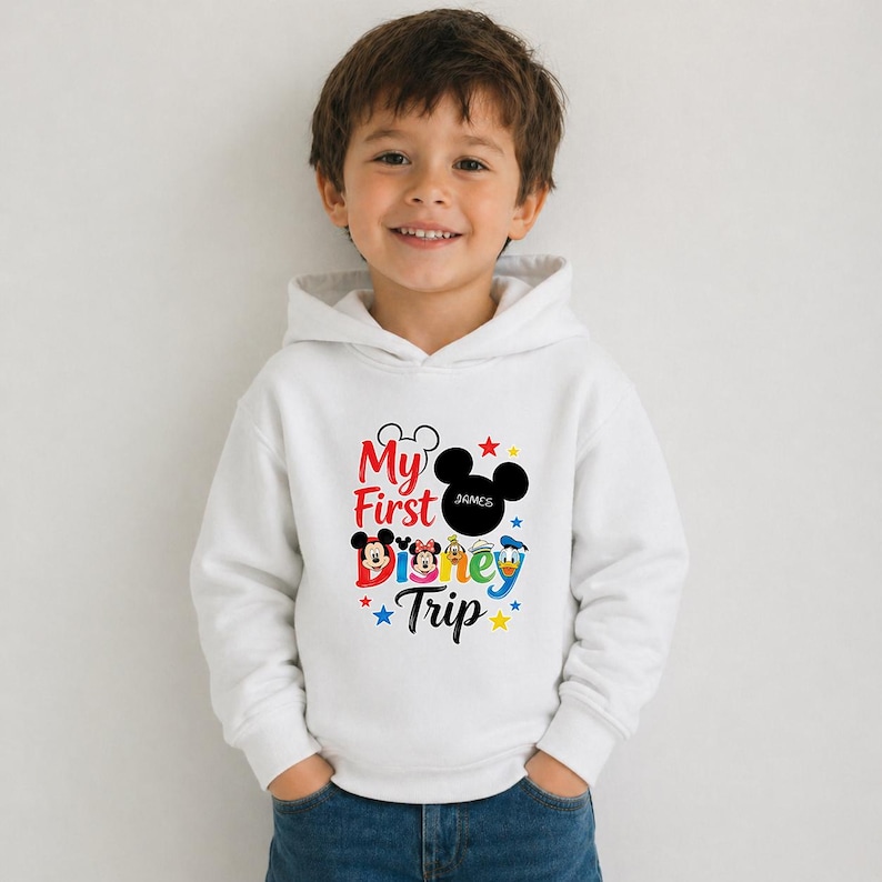 A young boy wearing a white hoodie with a Disney-themed graphic and text, smiling at the camera.