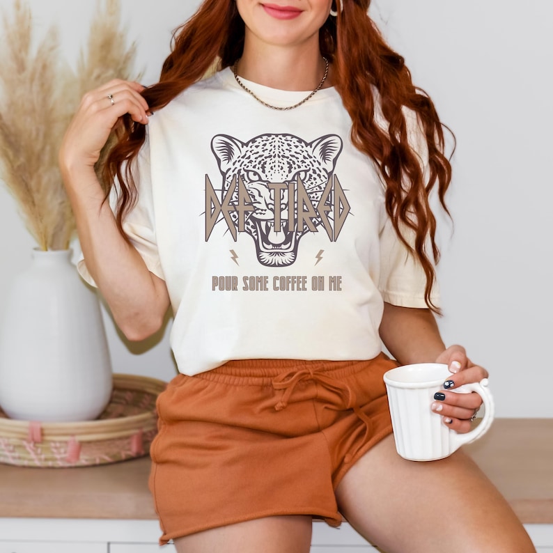 May include: A white t-shirt with a brown graphic of a leopard's head with the text "Retired" in brown letters above the head and "Pour some coffee on me" in brown letters below the head.