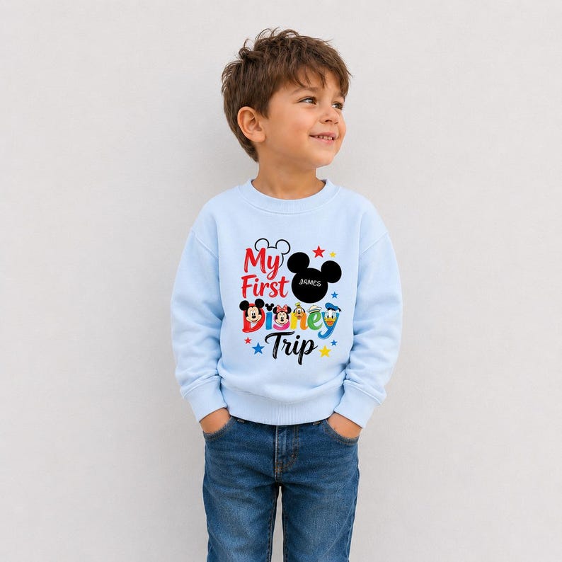 A young boy wearing a light blue sweatshirt with a Disney-themed design and text, smiling and looking up.