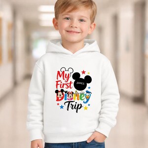 A young boy wearing a white hoodie with a Disney-themed graphic and text printed on it.
