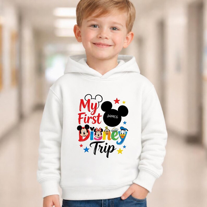 A young boy wearing a white hoodie with a Disney-themed graphic and text printed on it.