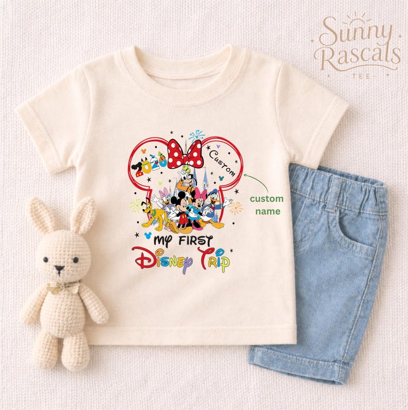 A white t-shirt with a Disney-themed graphic and a small stuffed bunny rabbit, along with a pair of blue denim shorts, are displayed on a white background.