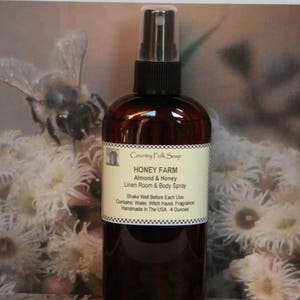 May include: A brown glass bottle with a black spray nozzle and a white label that reads "Country Folk Soap Honey Farm Almond & Honey Linen Room & Body Spray Shake Well Before Each Use Contains: Water, Witch Hazel, Fragrance Handmade In The USA 4 Ounces".