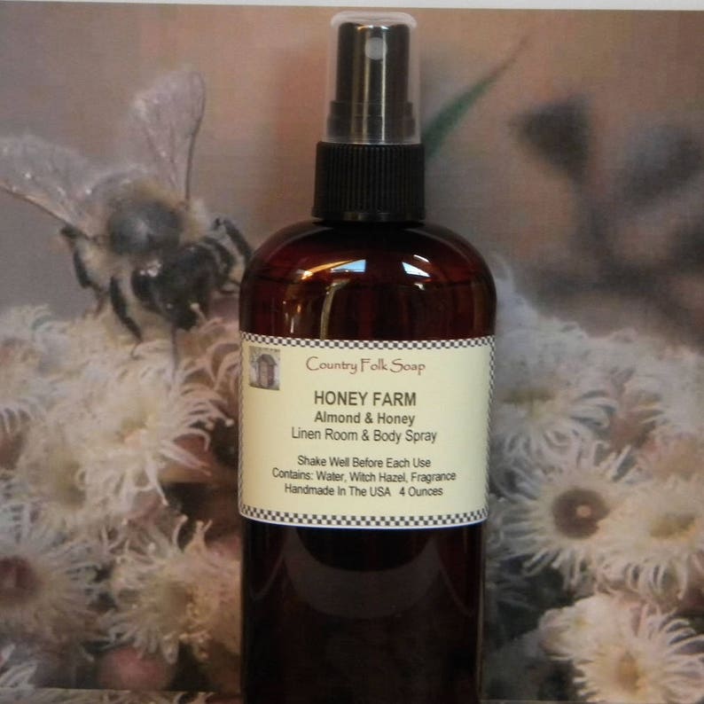 May include: A brown glass bottle with a black spray nozzle and a white label that reads "Country Folk Soap Honey Farm Almond & Honey Linen Room & Body Spray Shake Well Before Each Use Contains: Water, Witch Hazel, Fragrance Handmade In The USA 4 Ounces".