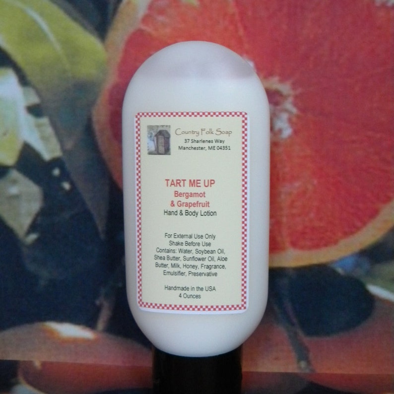 May include: A white bottle of hand and body lotion with a label that reads "Tart Me Up Bergamot & Grapefruit Hand & Body Lotion". The label also includes the name "Country Folk Soap" and the address "37 Sharienes Way Manchester, ME 04351". The bottle is 4 ounces and is handmade in the USA.