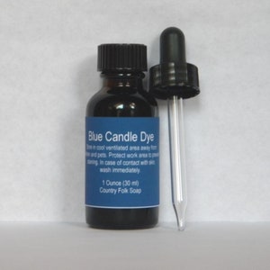 May include: A small glass bottle with a dropper filled with blue candle dye. The bottle has a black label with the text "Blue Candle Dye" and instructions for use. The label also states "1 Ounce (30 ml) Country Folk Soap."