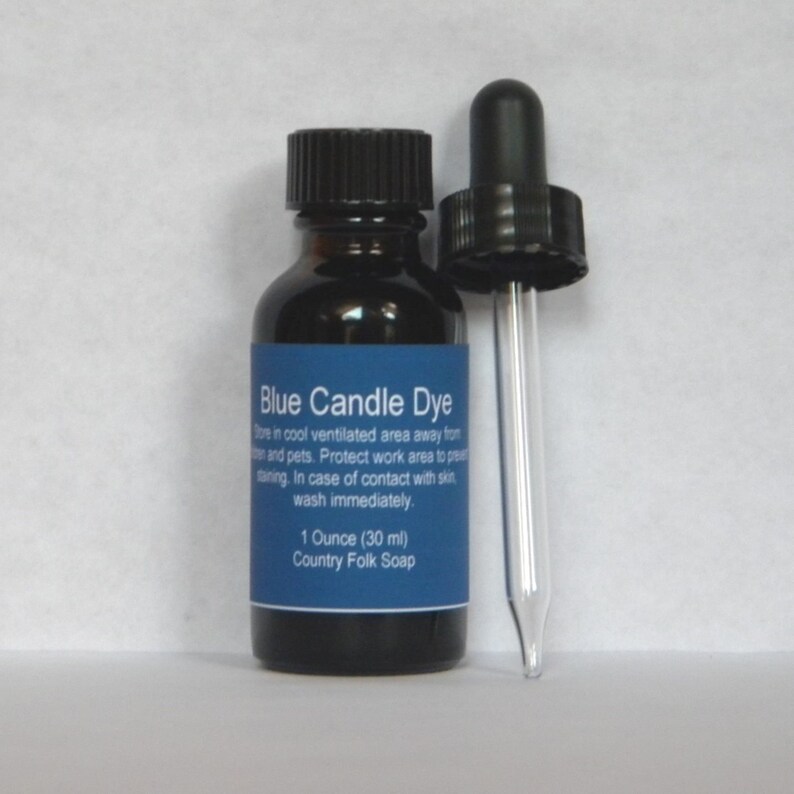 May include: A small glass bottle with a dropper filled with blue candle dye. The bottle has a black label with the text "Blue Candle Dye" and instructions for use. The label also states "1 Ounce (30 ml) Country Folk Soap."