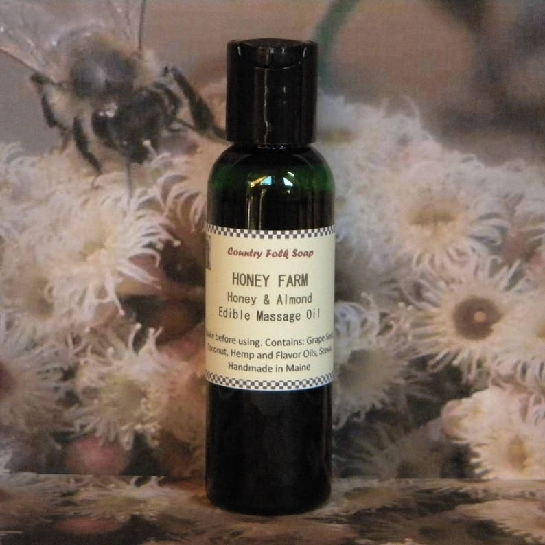 May include: A dark green glass bottle with a black cap and a white label that reads "Country Folk Soap Honey Farm Honey & Almond Edible Massage Oil" and "Handmade in Maine".