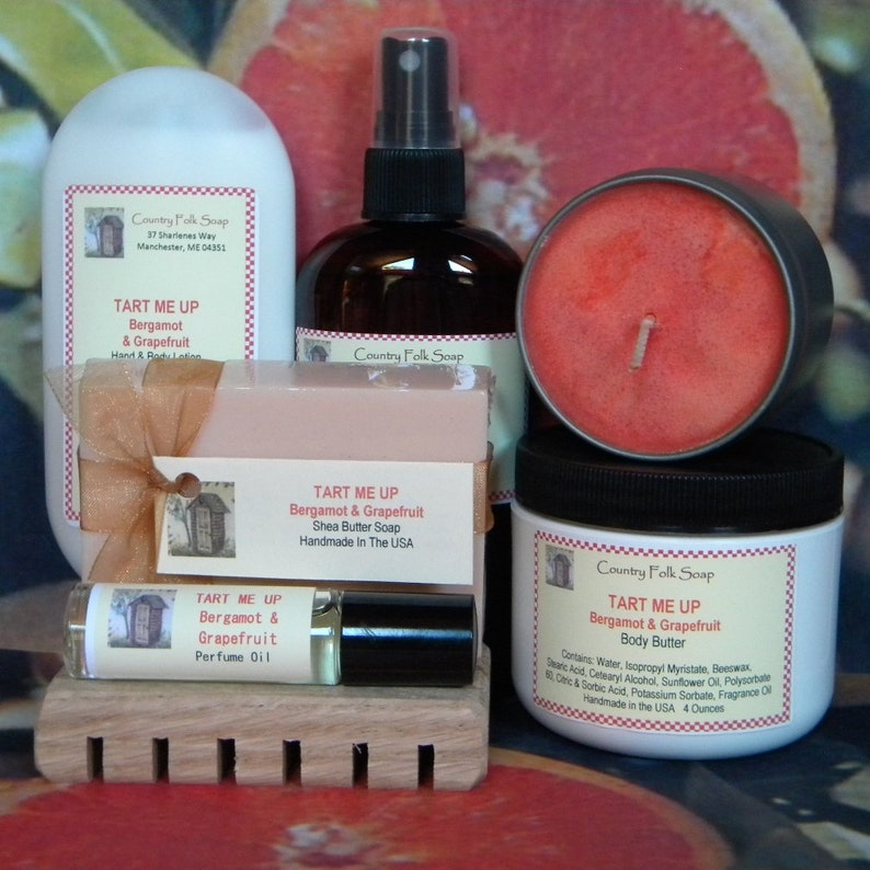 May include: A set of bath and body products with a bergamot and grapefruit scent. The set includes a bar of soap, a bottle of body butter, a bottle of hand and body lotion, a bottle of perfume oil, and a candle. The products are all labeled with the text "Tart Me Up" and "Country Folk Soap".