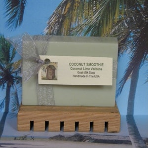 May include: A bar of green goat milk soap with a silver ribbon and a tag that reads "COCONUT SMOOTHIE Coconut Lime Verbena Goat Milk Soap Handmade In The USA".