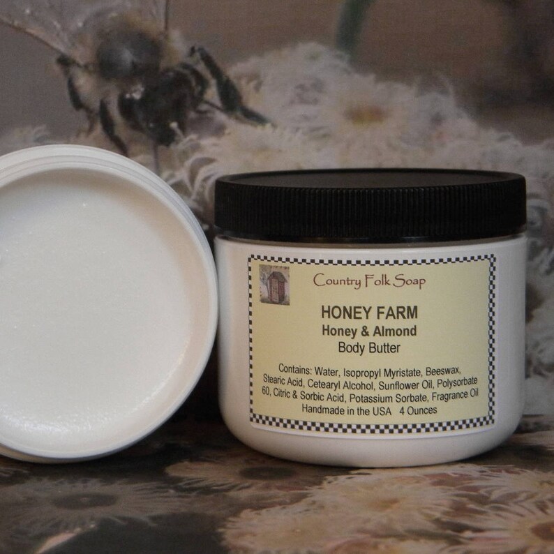 May include: A white jar with a black lid containing Honey Farm Honey & Almond Body Butter. The jar is labeled with the ingredients: Water, Isopropyl Myristate, Beeswax, Stearic Acid, Cetearyl Alcohol, Sunflower Oil, Polysorbate 60, Citric & Sorbic Acid, Potassium Sorbate, Fragrance Oil. The jar is handmade in the USA and contains 4 ounces of body butter.