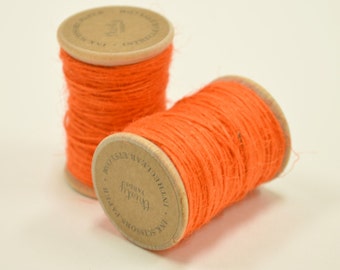 Puede incluir: Dos carretes de hilo naranja brillante, cada uno envuelto alrededor de un carrete de cartón con una etiqueta marrón que dice "The Scissors Paper", "Handmade", "Twine" y "Professionally Woven".