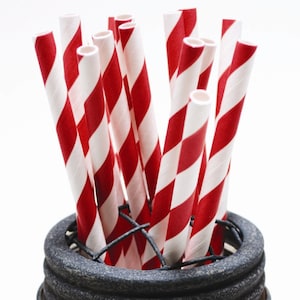 May include: A close-up of a group of red and white striped paper straws in a black metal holder.