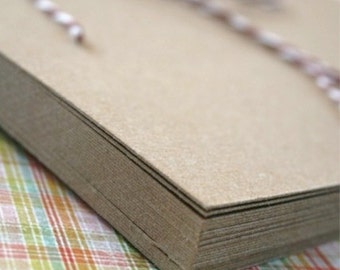 May include: A stack of brown cardstock paper with a white and brown twine tied around it. The paper is on a plaid fabric surface.