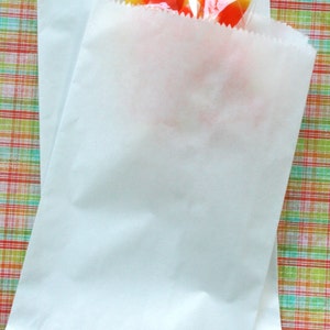 May include: Two white paper bags with a clear plastic bag of orange and yellow candy corn inside.