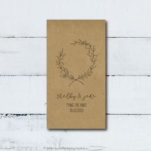 May include: A brown paper card with a simple wreath design and the text "Shelby & Jake Tying the Knot 10.03.2020"
