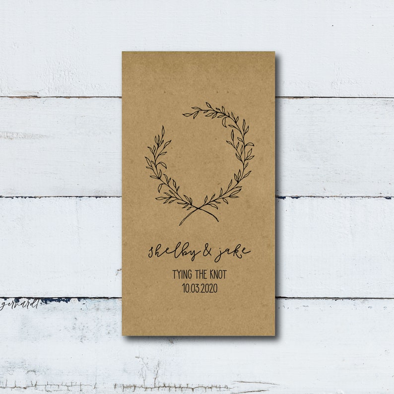 May include: A brown paper card with a simple wreath design and the text "Shelby & Jake Tying the Knot 10.03.2020"