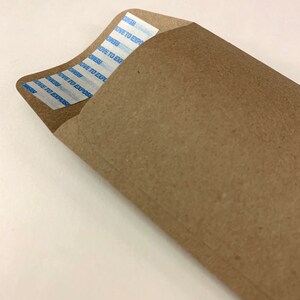 以下が含まれることがあります： 白い粘着テープが貼られた茶色の紙の封筒。テープには「REMOVE TO EXPOSE」という文字が複数回繰り返されている。