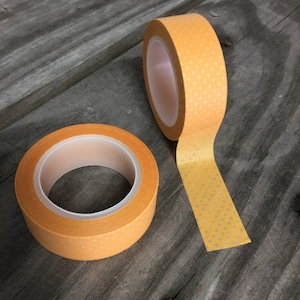 May include: Two rolls of orange washi tape with white polka dots. The tape is rolled up and one roll is unrolled.