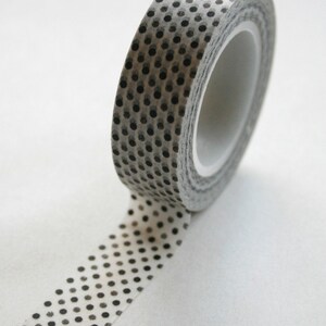 May include: A roll of white washi tape with a black polka dot pattern. The tape is rolled up and a portion of the tape is unrolled.
