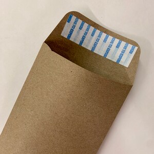 以下が含まれることがあります： 「REMOVE TO EXPOSE」という文字が複数回書かれた青と白のセキュリティストリップが付いた茶色の紙の封筒です。