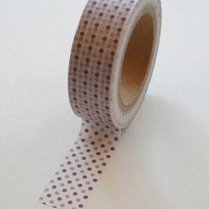 May include: A roll of washi tape with a white background and a purple polka dot pattern. The dots are a gradient of purple, with the darkest purple at the top of the roll and the lightest purple at the bottom.