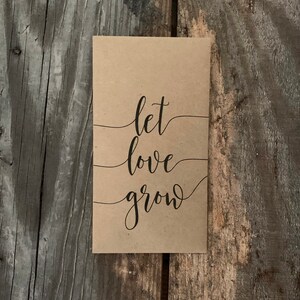 以下が含まれることがあります： 黒い筆記体で「let love grow」と書かれた茶色の紙のカードです。