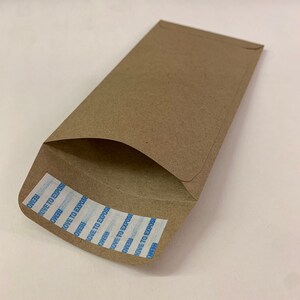 以下が含まれることがあります： REMOVE TO EXPOSEと書いてある青と白の粘着テープが付いた茶色の紙の封筒です。