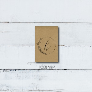 May include: A brown paper favor bag with a black and white design. The design features a floral wreath with the letter "H" in the center. The text "Jill & Jerome Helm 12.21" is written around the wreath.