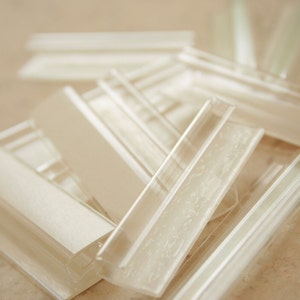 May include: A close-up of a pile of clear plastic trim pieces. The pieces are all rectangular and have a smooth, glossy finish.