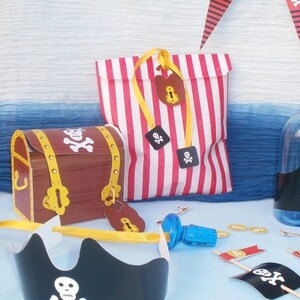 Peut inclure: Un ensemble de cadeaux de f&ecirc;te sur le th&egrave;me des pirates avec un sac en papier &agrave; rayures rouges et blanches, un coffre au tr&eacute;sor en carton marron, un chapeau de pirate noir et des pi&egrave;ces d'or. L'ensemble comprend &eacute;galement une bouteille en plastique bleue avec un bouchon et un petit drapeau avec un cr&acirc;ne et des os crois&eacute;s.
