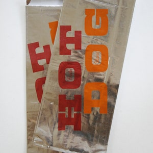 May include: Two silver foil food pouches with the word "FOOD" printed in red and orange letters. The text "Fresh" and "Delicious" are also printed on the pouches.