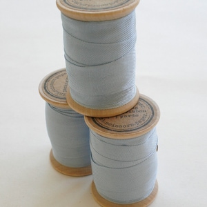 May include: Three spools of light blue ribbon with brown labels. The labels have text that reads "The Paper Scissors - 1 yard ribbon -  The Paper Scissors - 1 yard ribbon - The Paper Scissors - 1 yard ribbon".