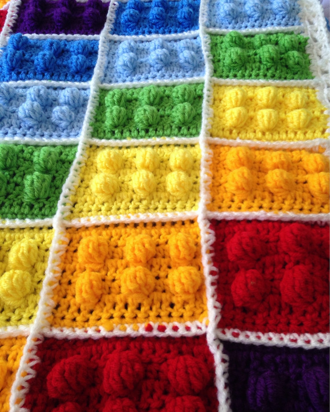 Close-up of a LEGO-inspired crochet blanket with colorful “brick” squares and white joining