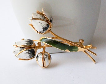 May include: A gold-toned brooch with three white and black enamel tulips. The tulips have green enamel stems and leaves.