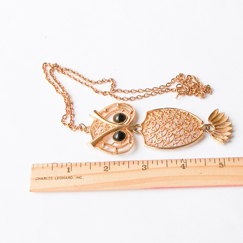 May include: A gold-tone owl pendant necklace with black glass eyes. The pendant is made of filigree metal and is about 3 inches long. The necklace is about 20 inches long.