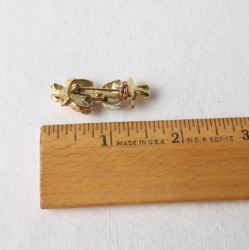 May include: A gold-toned brooch featuring blue and white enamel and rhinestones. The brooch is shaped like a bird with its wings outstretched. The brooch measures approximately 2.5 cm in length.