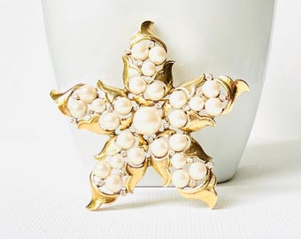May include: A gold-toned brooch in the shape of a starfish, adorned with faux pearls and rhinestones.