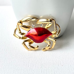 May include: A gold-tone crab brooch with red enamel and clear rhinestones.