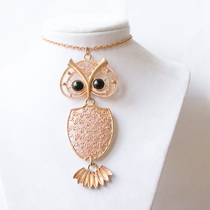 May include: Gold owl pendant necklace with black glass eyes. The owl is made of filigree metal and has a detailed design. The necklace is on a gold chain.