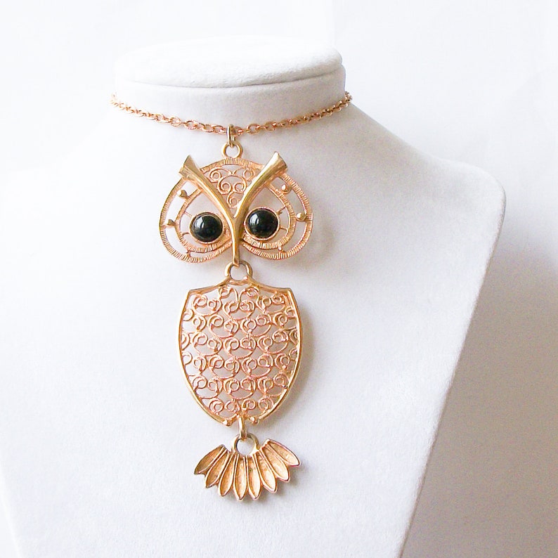 May include: Gold owl pendant necklace with black glass eyes. The owl is made of filigree metal and has a detailed design. The necklace is on a gold chain.
