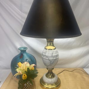 May include: A table lamp with a black lampshade, marble-patterned base, and gold accents. The lamp is paired with a blue vase and a small decorative pineapple-shaped container with flowers. The lamp's height is approximately 24 inches.