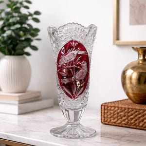 May include: Clear crystal vase with a ruby red oval center featuring etched birds on branches. The vase has a flared top and a detailed, patterned design. The vase is approximately 25 cm tall.