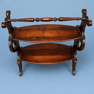 May include: A two-tiered, dark wood serving stand with a handle. The stand has two oval shelves and ornate, curved supports. The wood has a rich, warm tone, and the piece has a classic, antique aesthetic.